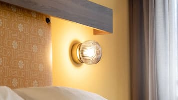 Quarto de hotel com cama, luminária na parede e quadro emoldurado sobre a cama.