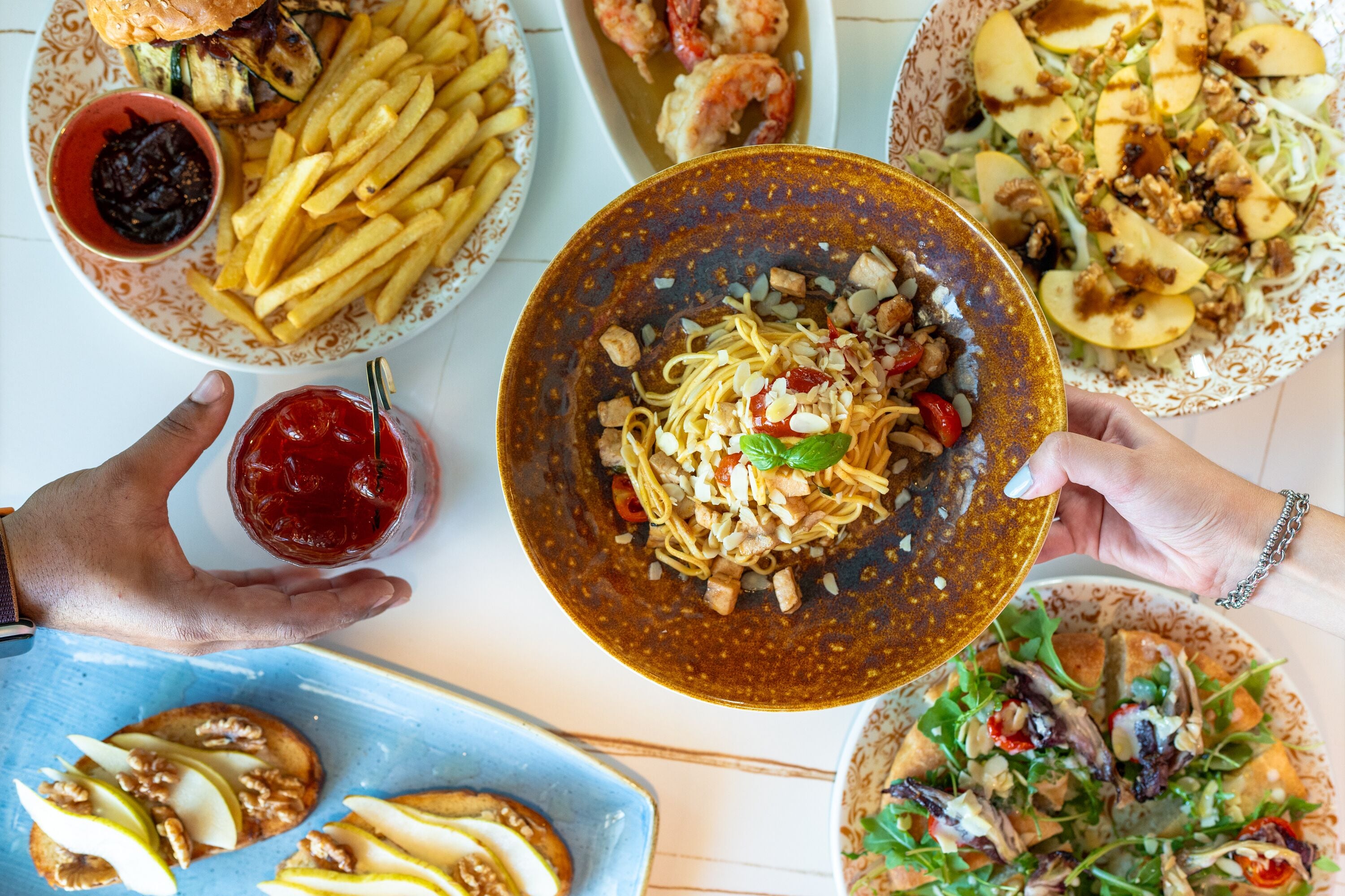 Diversos platos, como fideos, papas fritas y ensaladas, sugiriendo un ambiente de bufé o comida familiar.