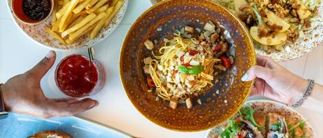 A variety of dishes including noodles, fries, and salads, suggesting a buffet or family meal setting.