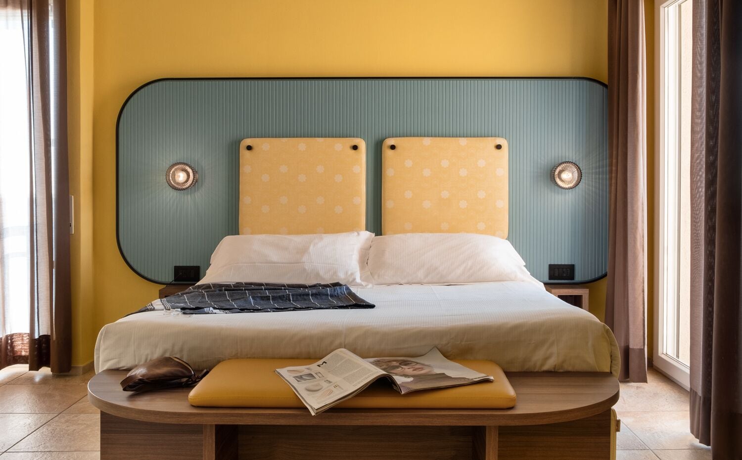 Una cama con cabecera, una mesita de noche y una ventana con cortinas.