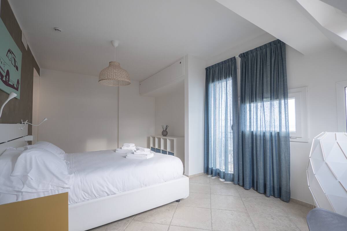 A modern bedroom with a large bed, a bedside table, a lamp, and a window with curtains.
