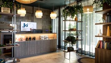 A modern reception area with a wooden counter, a digital screen displaying 'Jo' branding, and a large window with curtains.