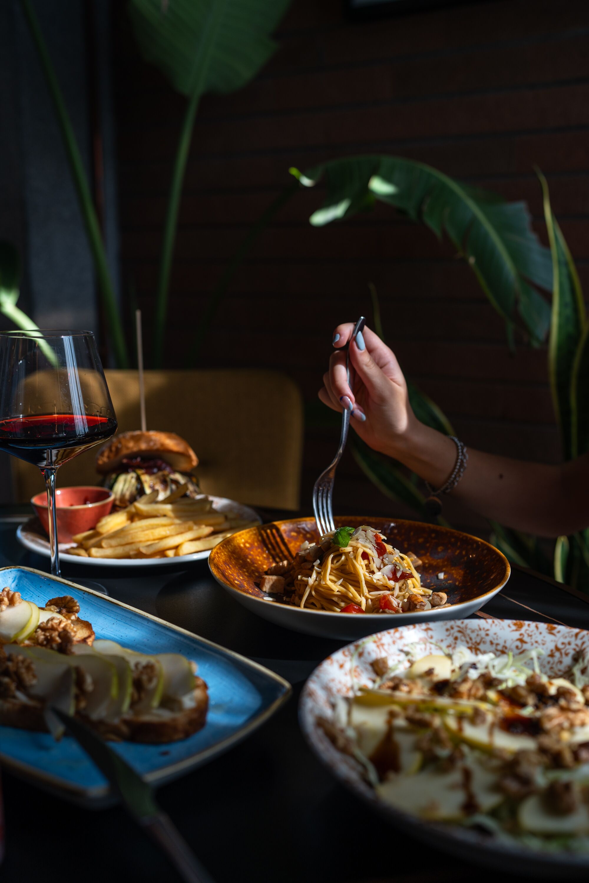 A dining table with various dishes, including pasta, a burger, and a glass of red wine.