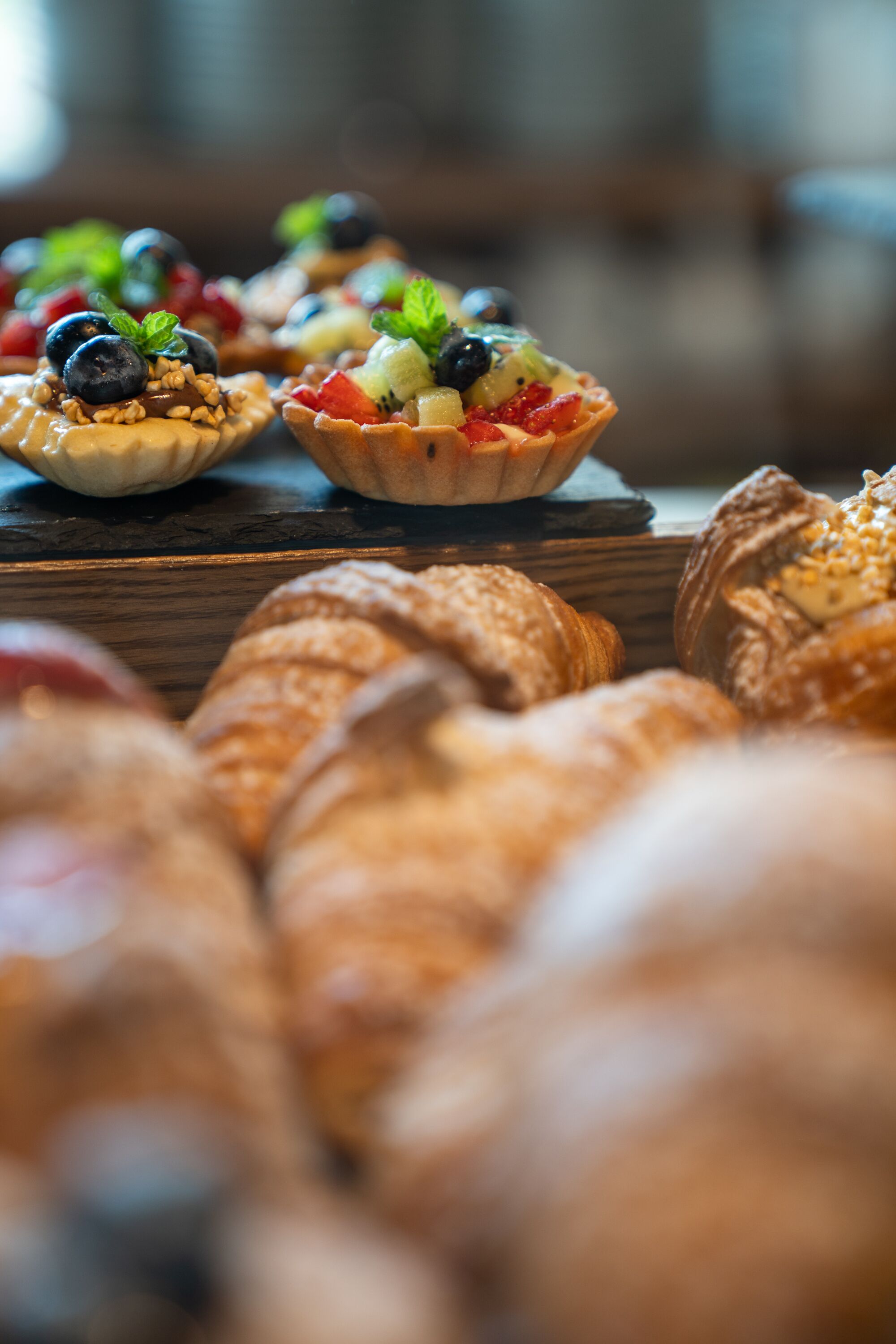 Eine Auswahl an Gebäck und Desserts, darunter Obsttorten und Croissants, präsentiert auf einer Holzoberfläche.