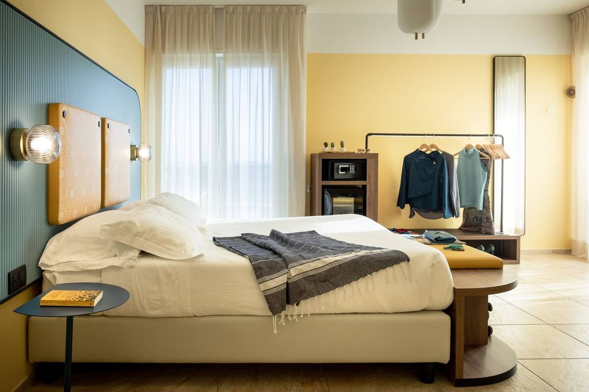 A hotel room with a bed, bedside table, and a mirror.