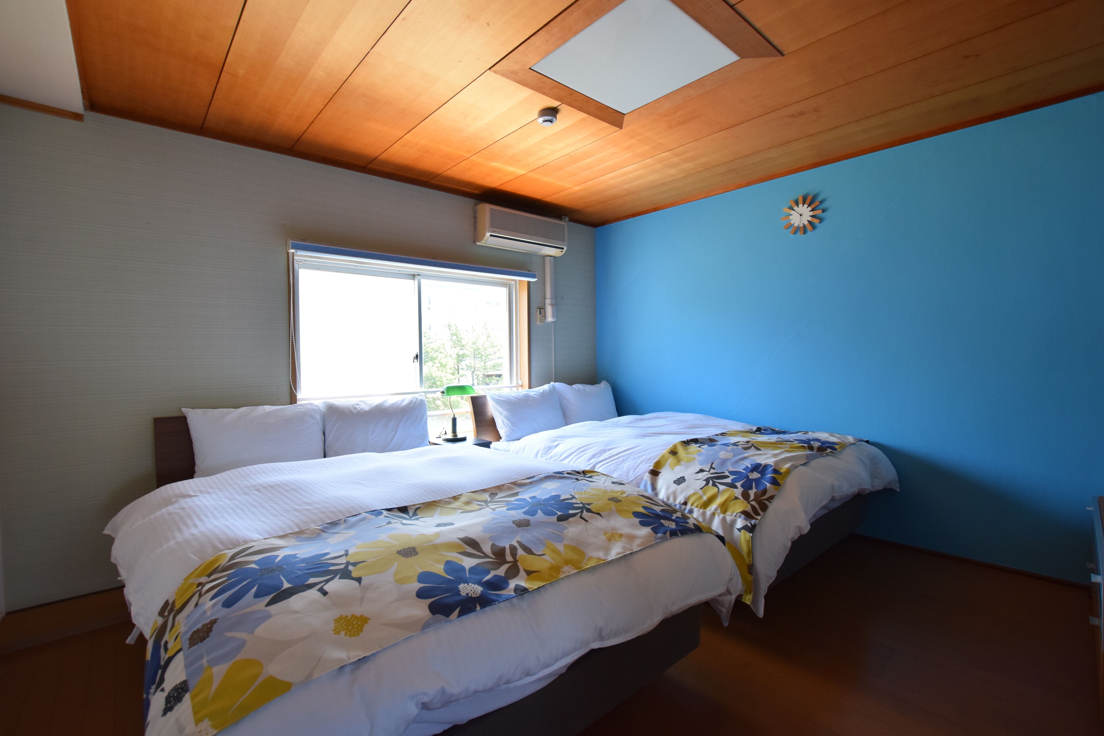 A bedroom with two beds, a window, an air conditioner, and a clock on the wall.