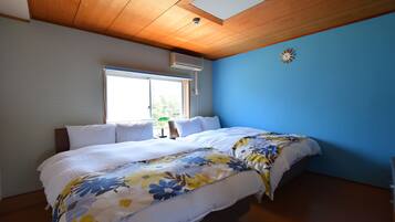 A bedroom with two beds, a window, an air conditioner, and a clock on the wall.