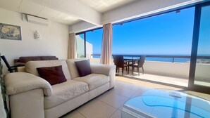 Un soggiorno moderno con un divano color beige, un tavolino in vetro e vista sull'oceano.