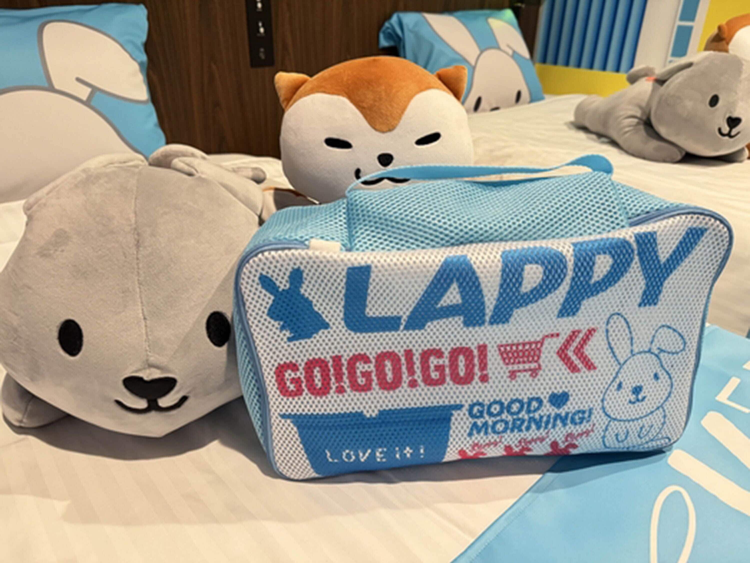 A bed with plush toys and a blue and white bag with text.