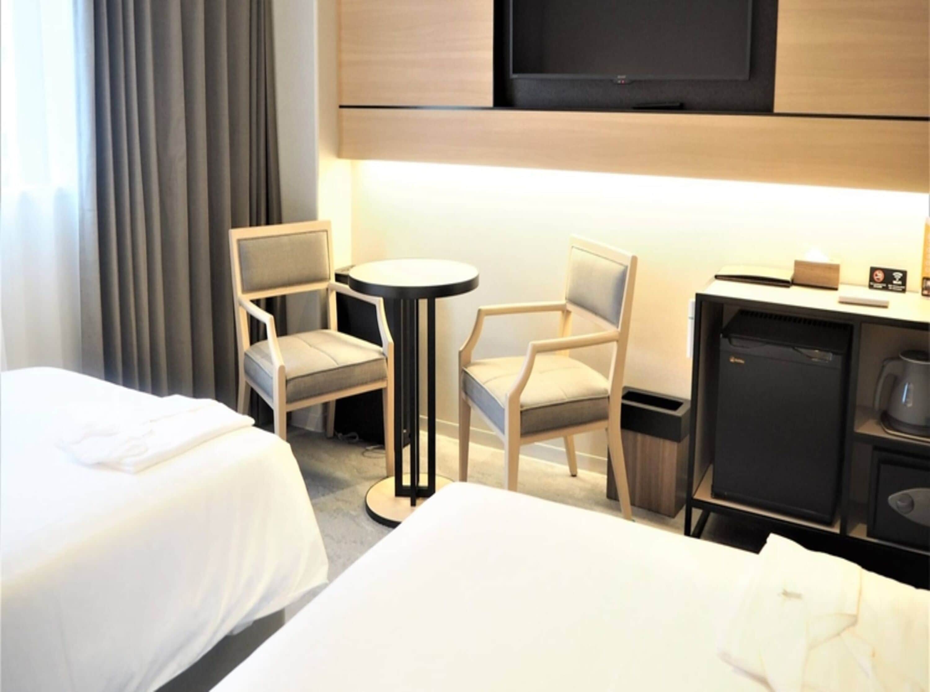 Une chambre d’hôtel avec deux lits, une petite table, deux chaises, un téléviseur, un minibar et une machine à café.