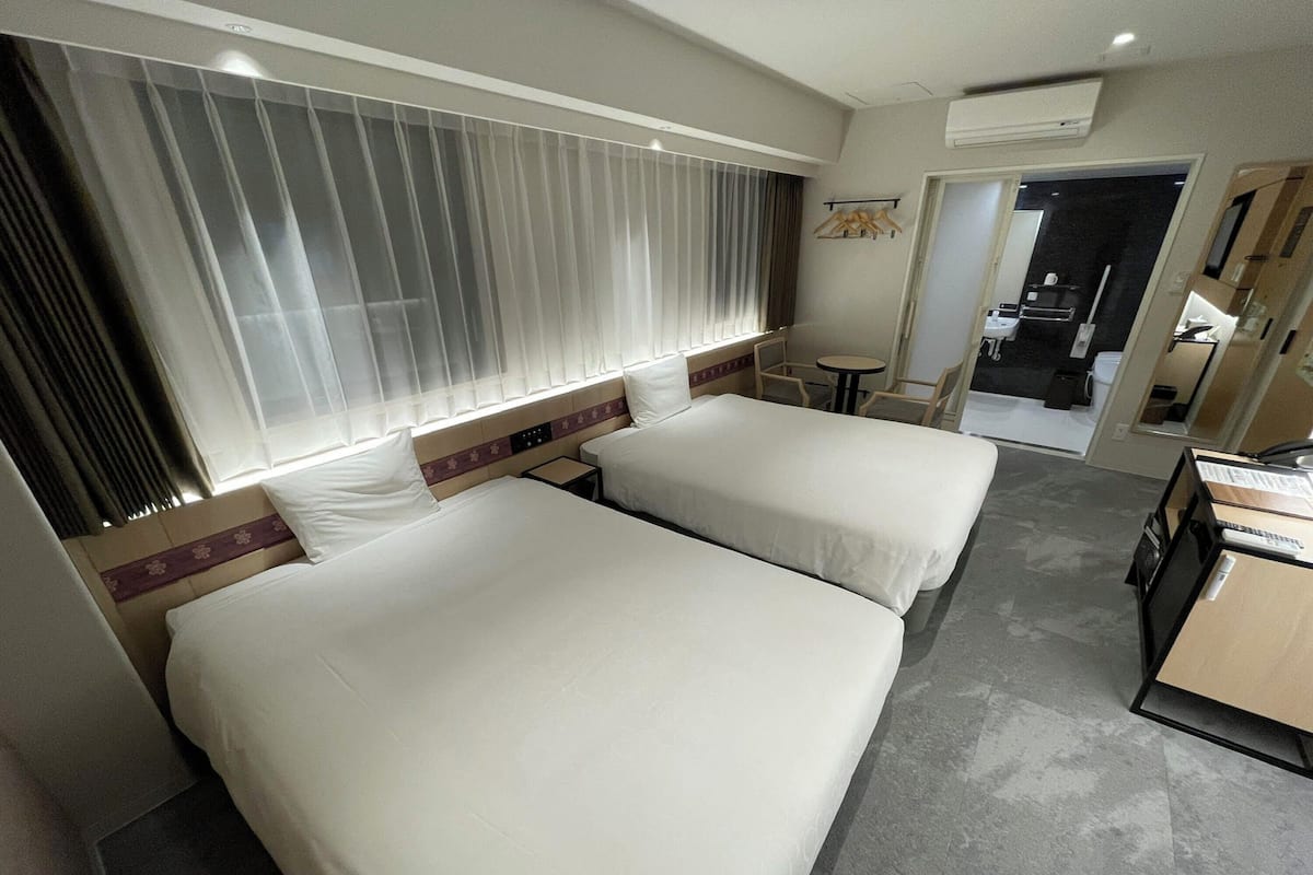 A hotel room with two beds, a small table, and a desk.