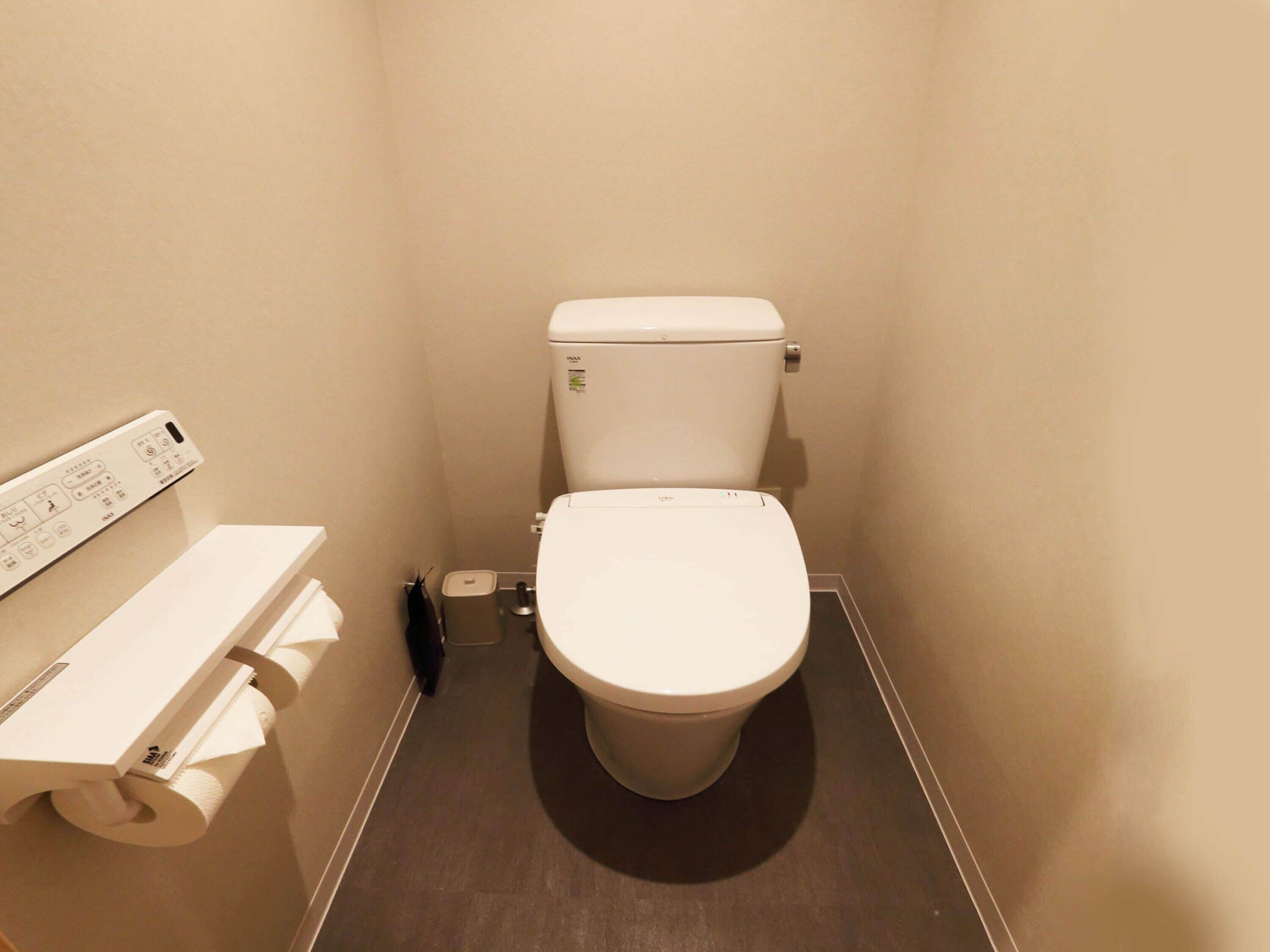 Baño pequeño y compacto con inodoro, dispensador de papel higiénico y panel de control en la pared.
