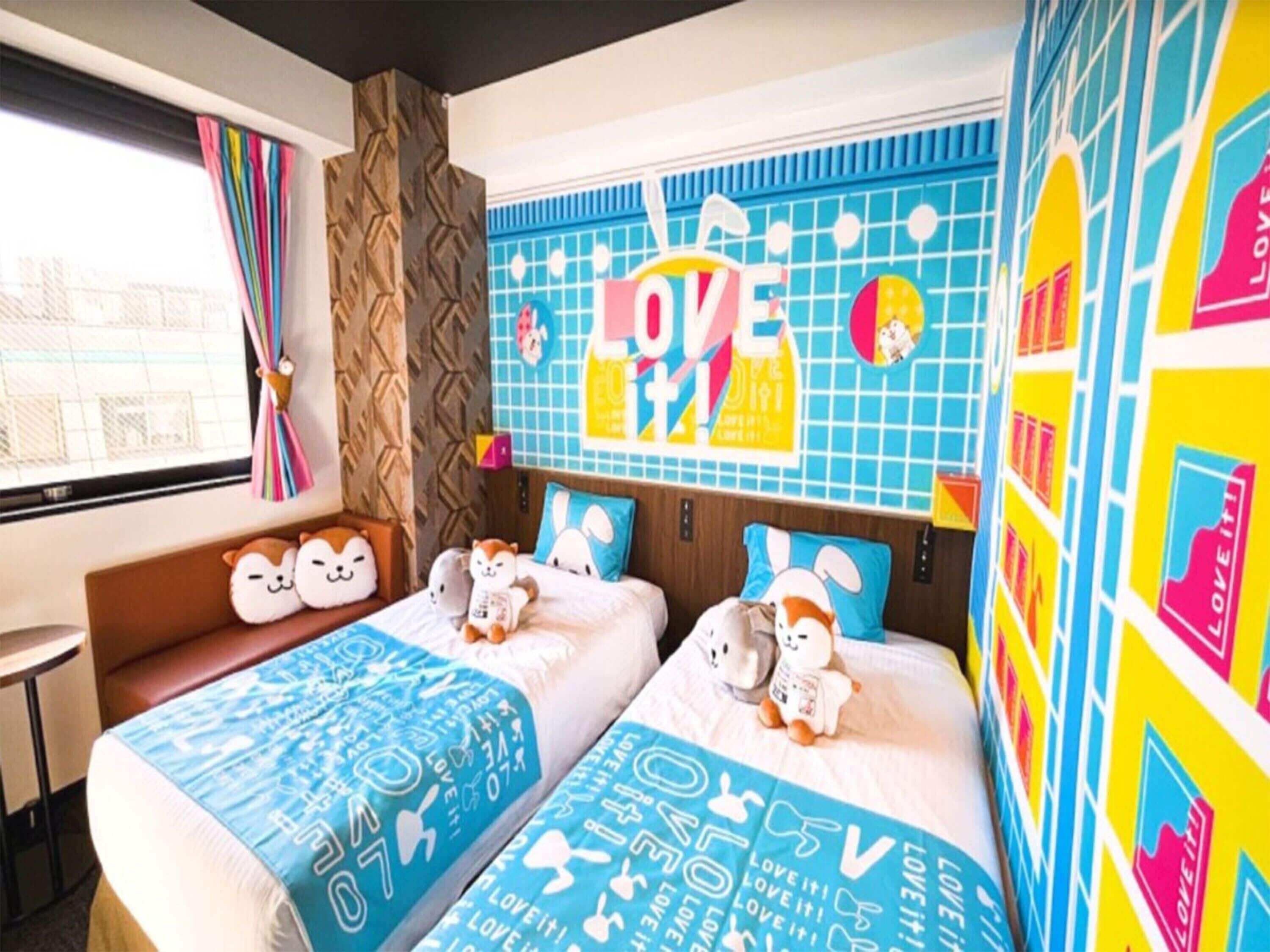 Quarto de hotel com duas camas, arte nas paredes em cores vibrantes e uma janela com cortinas.