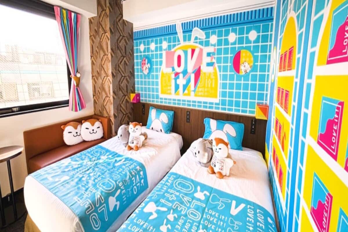 A hotel room with two beds, colorful wall art, and a window with curtains.
