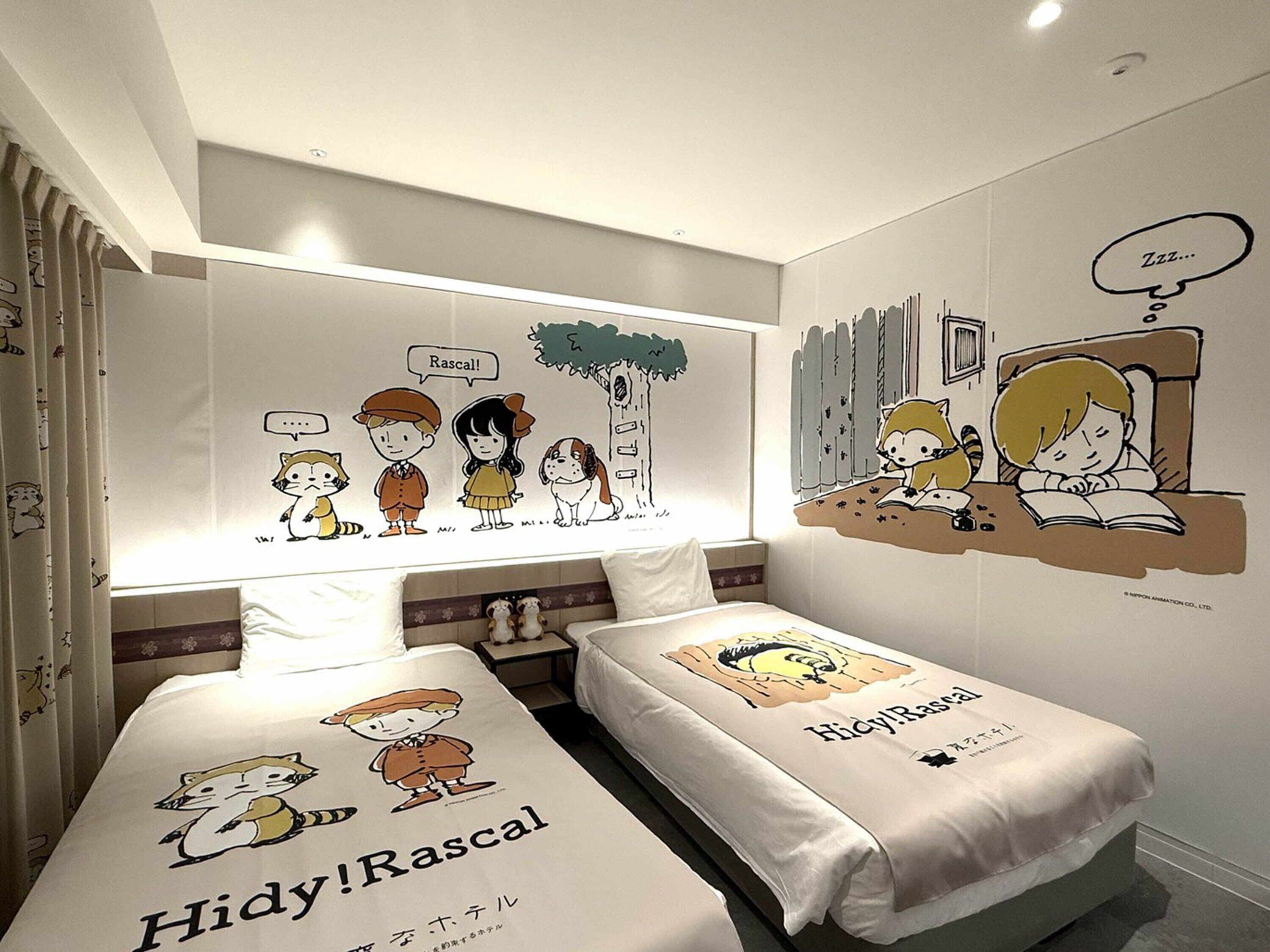 Quarto de hotel com duas camas, cada uma com colcha temática Hidy!Rascal, um grande mural na parede retratando personagens e uma janela com cortinas.
