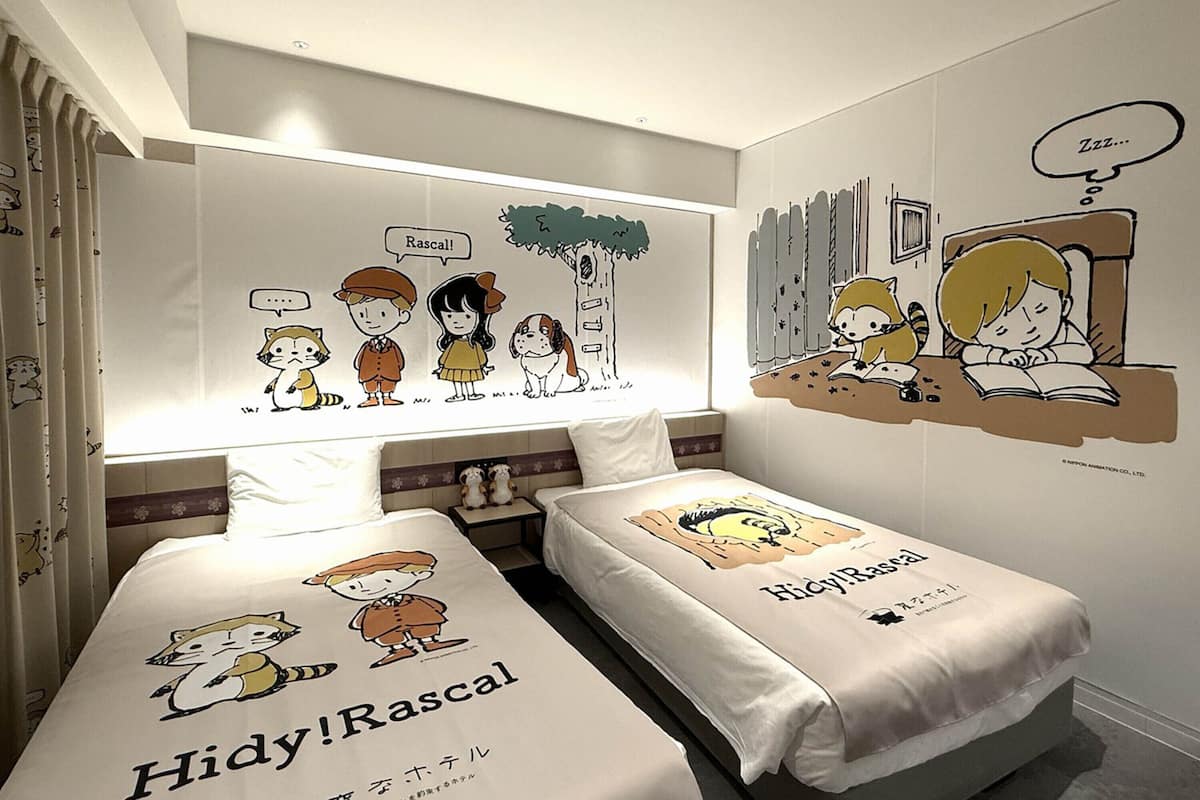 A hotel room with two beds, each with a Hidy!Rascal themed bedspread, a large wall mural depicting characters, and a window with curtains.