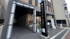 A hotel entrance with a modern facade, large glass windows, and a prominent signboard. - Henn na Hotel Premier Nara (Nara)