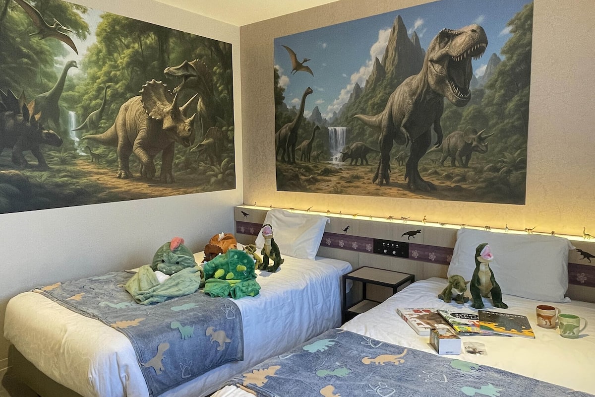A hotel room with two beds, dinosaur-themed bedding, and large dinosaur murals on the walls.