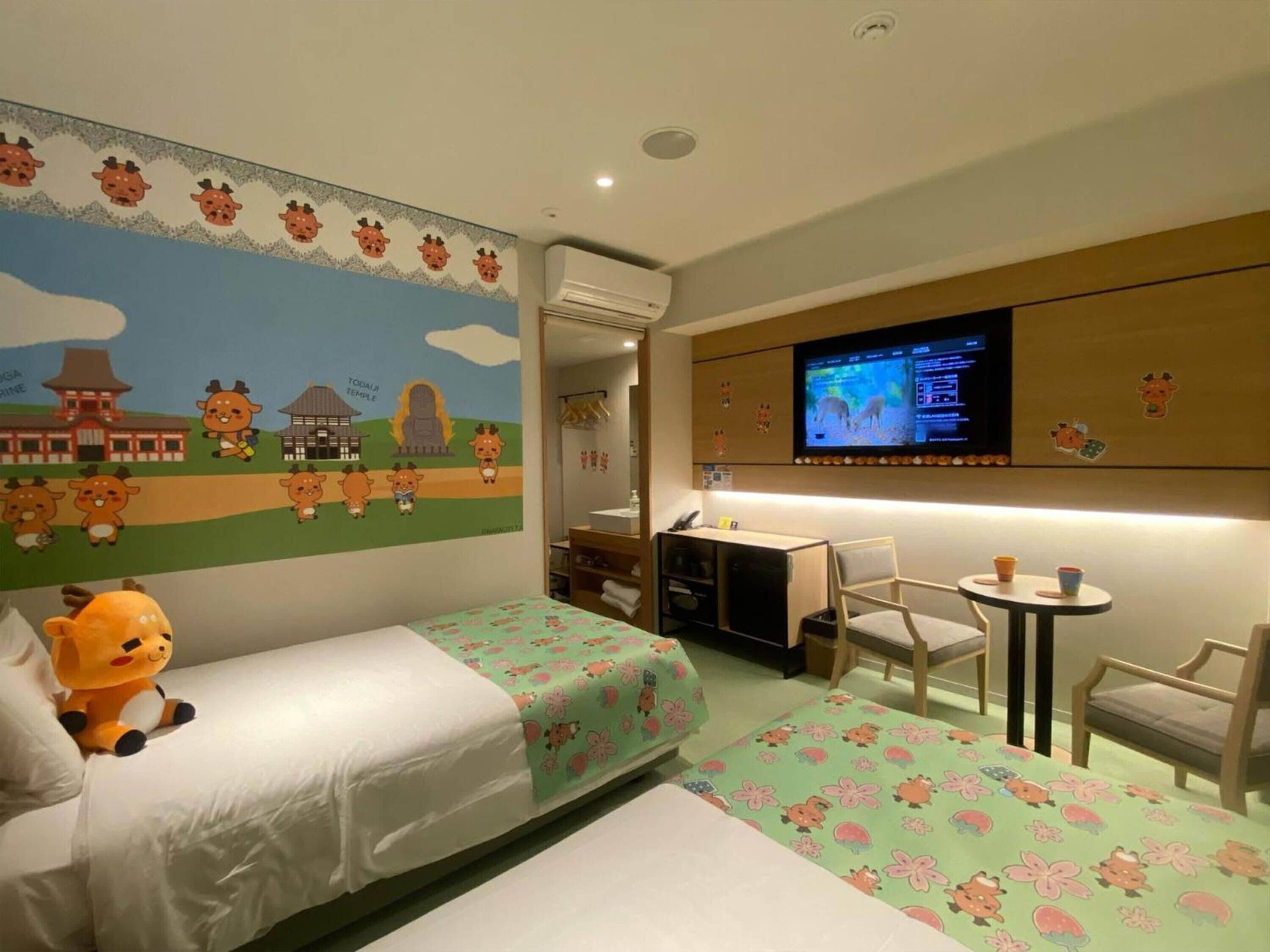 Quarto de hotel com duas camas, uma escrivaninha, uma cadeira, uma televisão e um mural na parede.