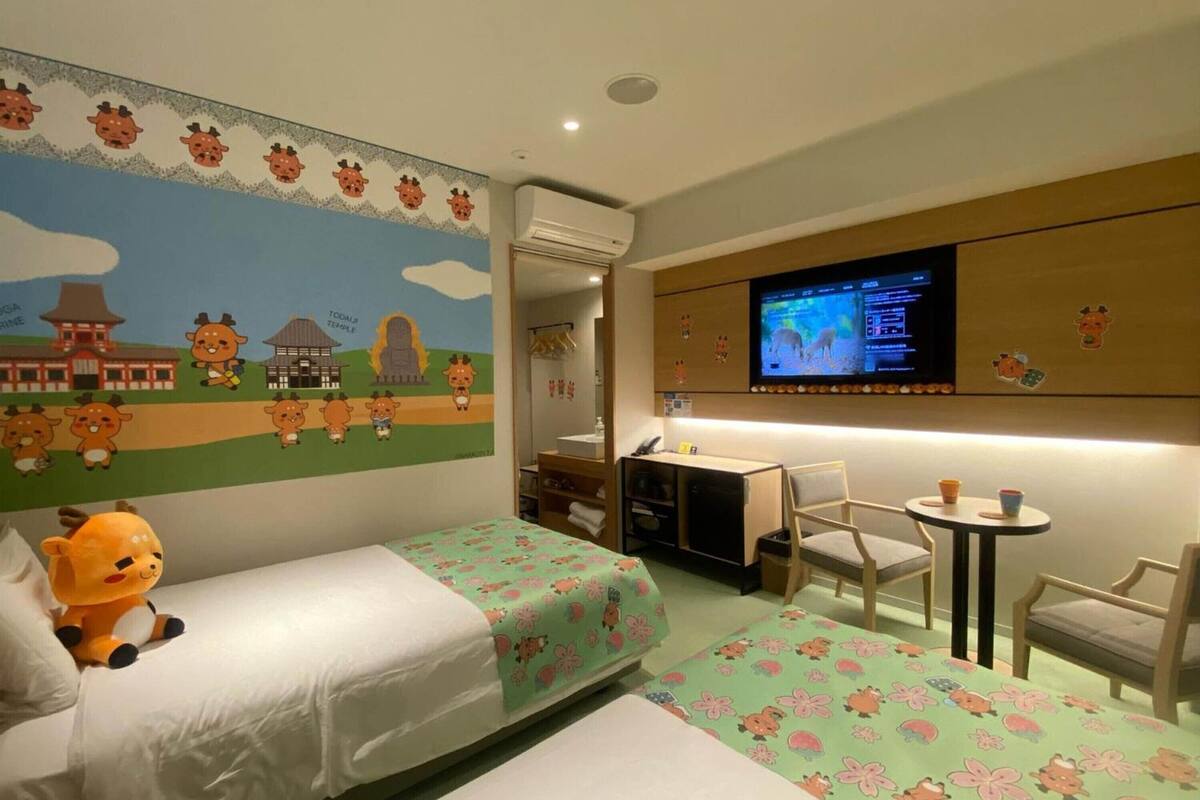 A hotel room with two beds, a desk, a chair, a television, and a mural on the wall.