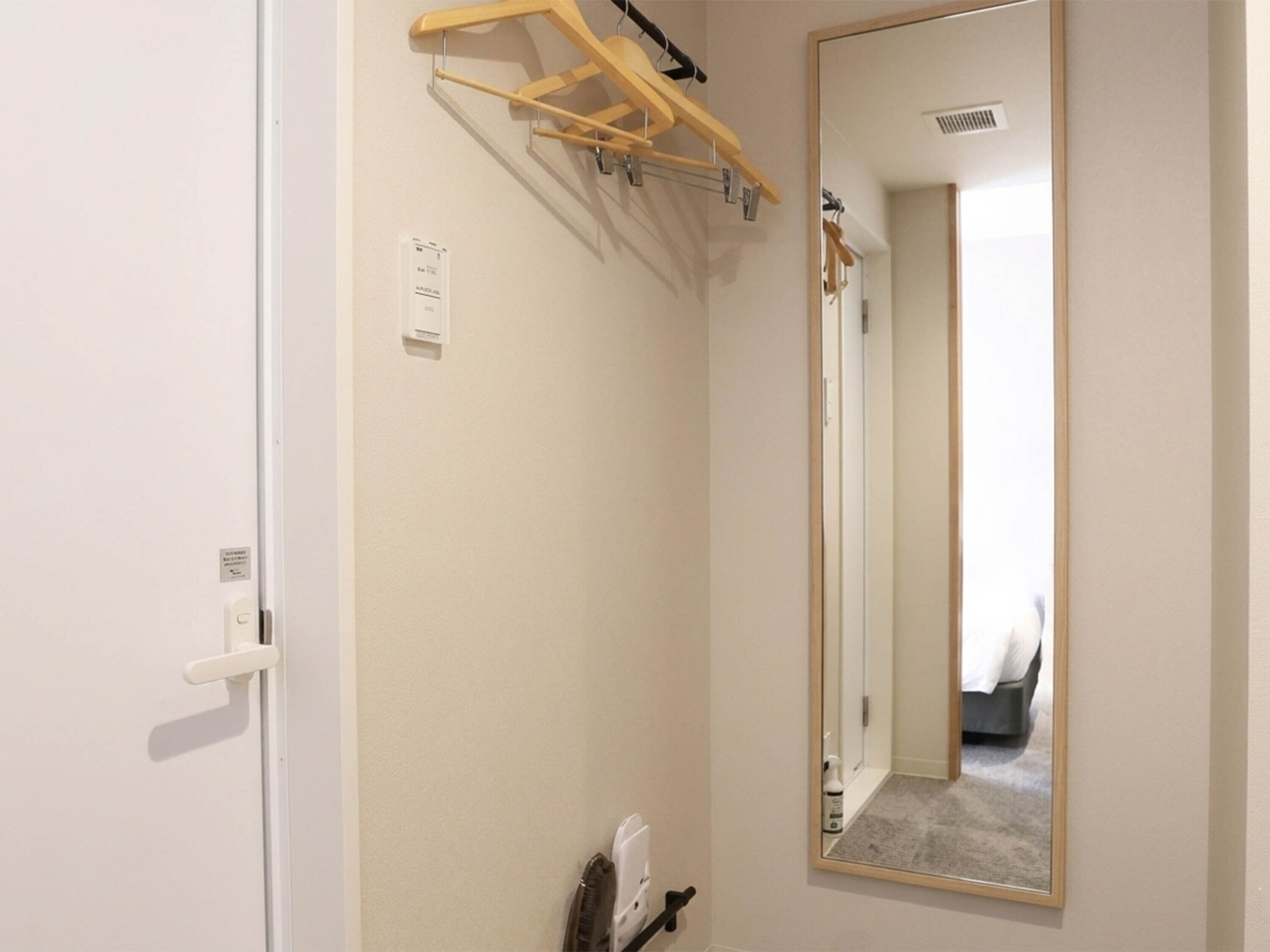 A hotel room with a door, a mirror, a towel rack, and a radiator.