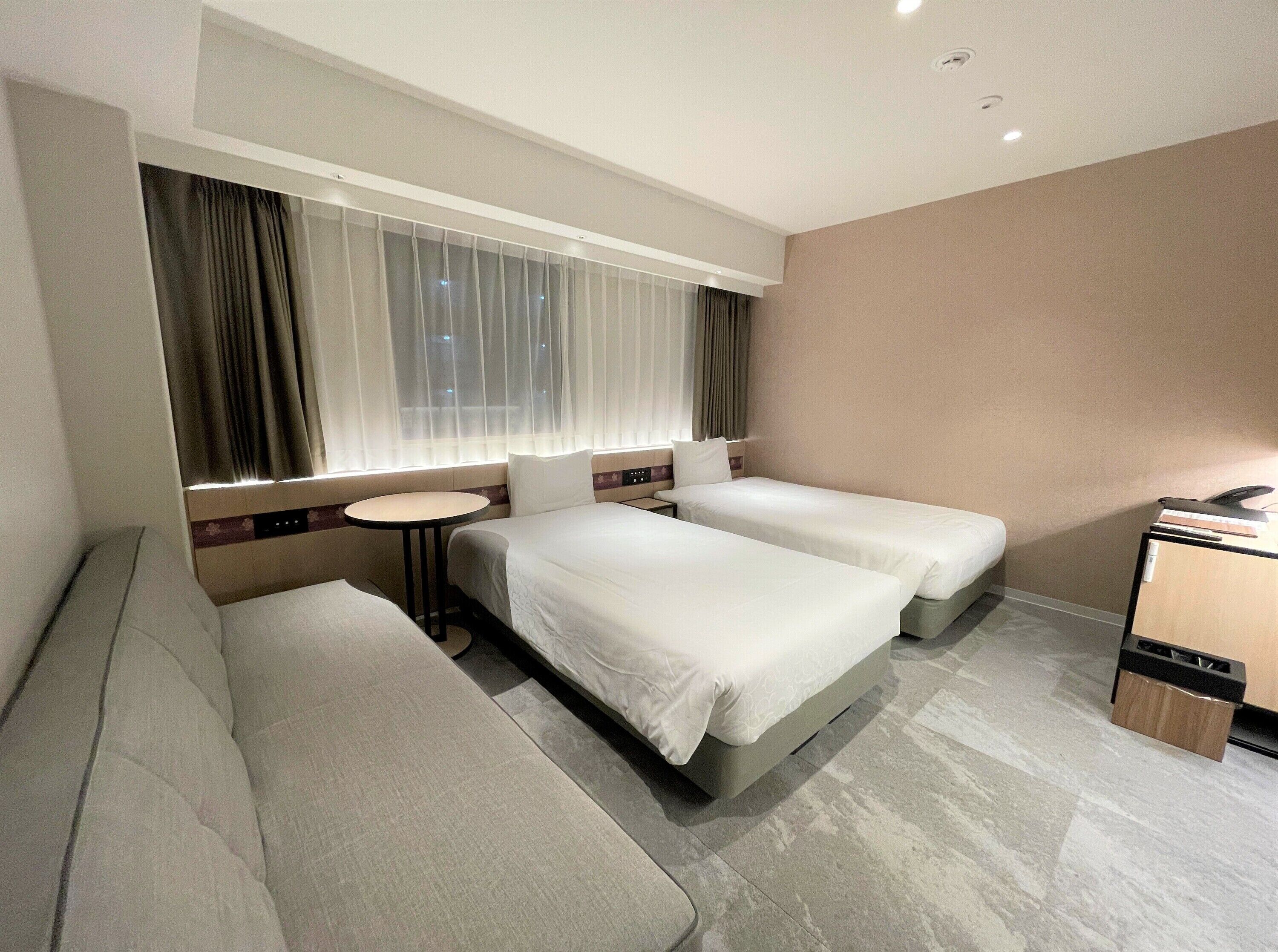 A hotel room with two beds, a sofa, a small table, and a desk.