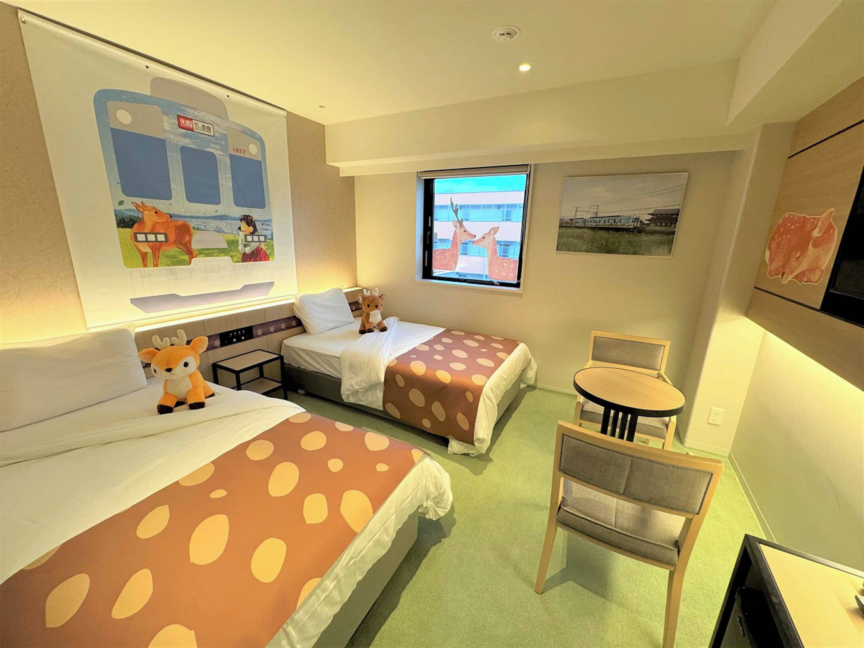 Quarto de hotel com duas camas, uma mesinha, uma cadeira, televisão e janela com vista.