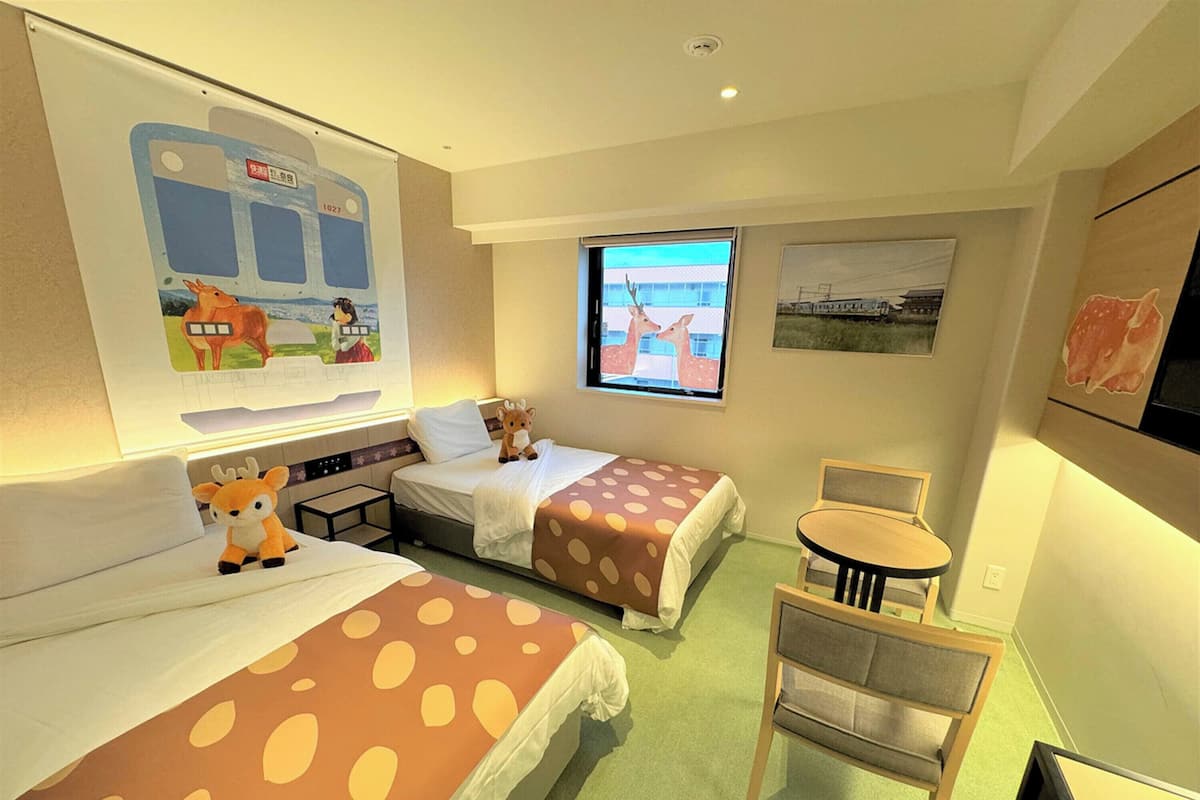 A hotel room with two beds, a small table, a chair, a TV, and a window with a view.
