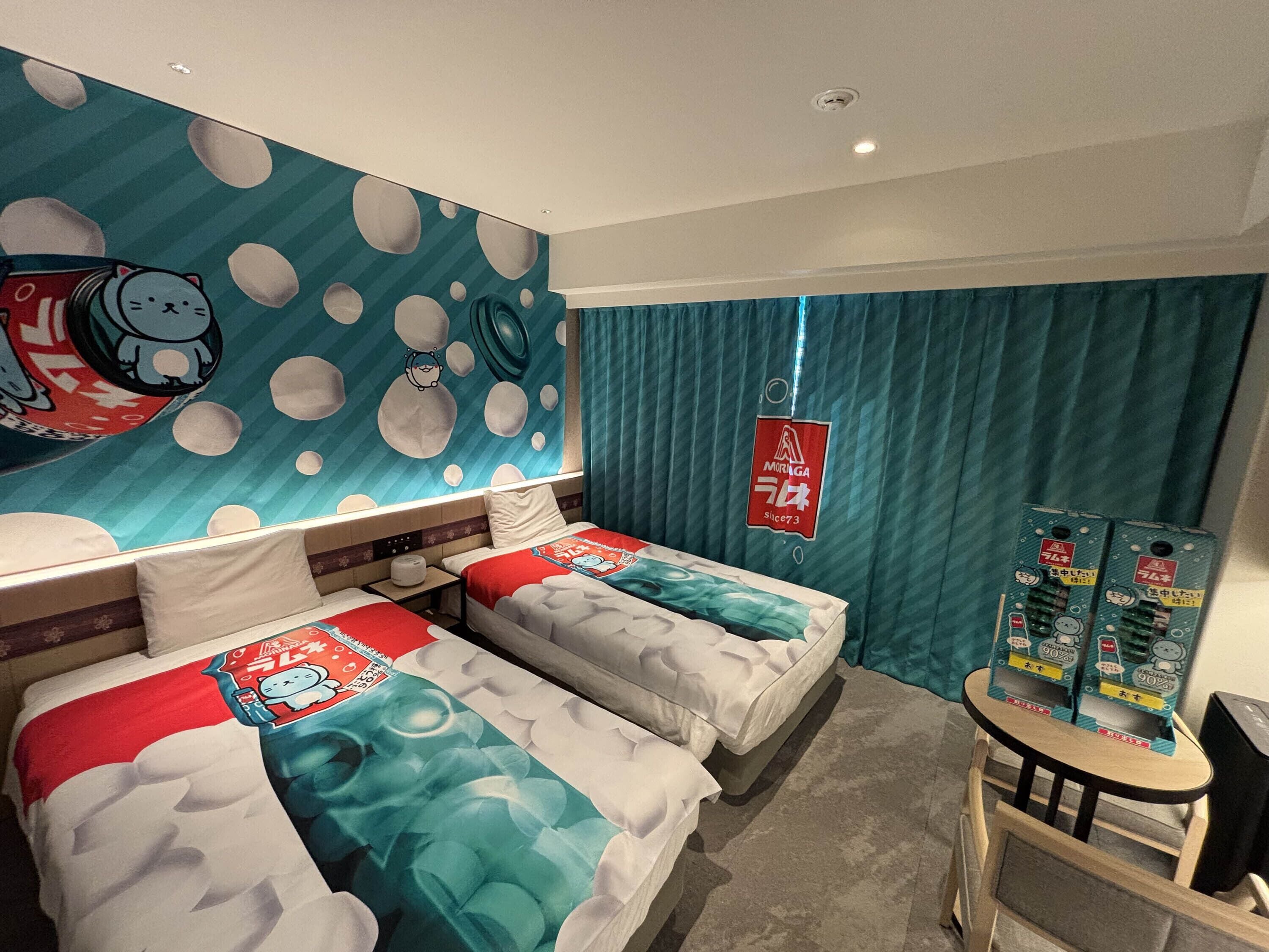 Quarto de hotel com duas camas, um mural na parede, uma mesinha e uma cortina.