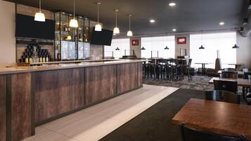 Un bar moderno con mostrador de madera, lámparas colgantes y una zona de estar con mesas y sillas.