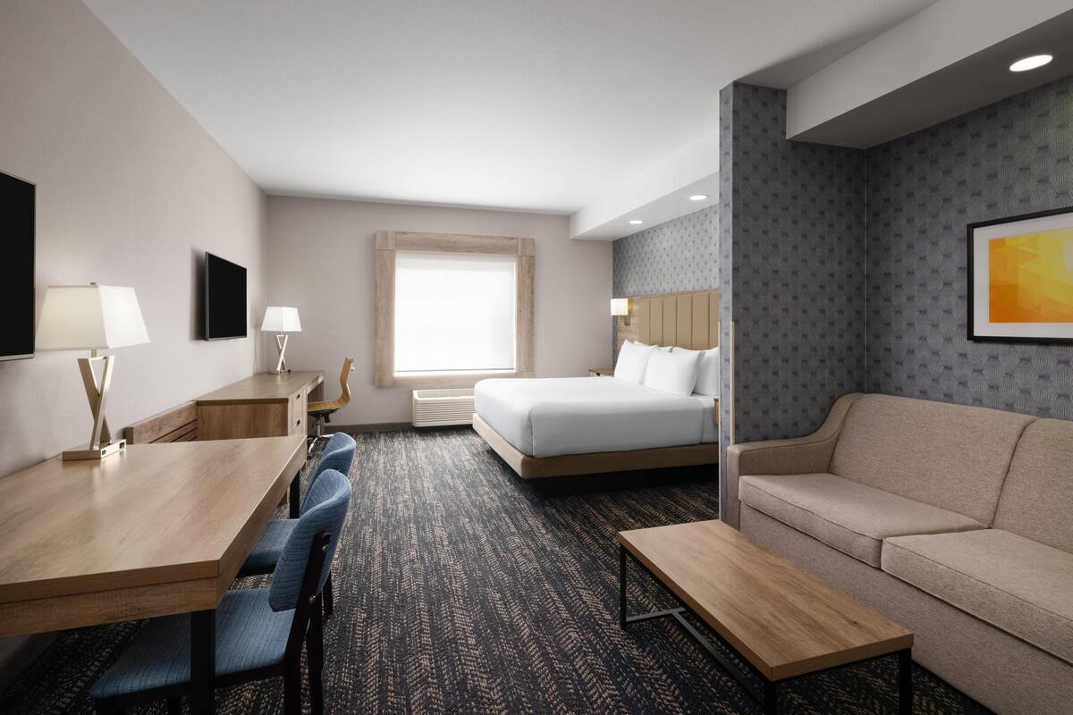 A hotel room with a bed, a sofa, a desk with chairs, and a TV.