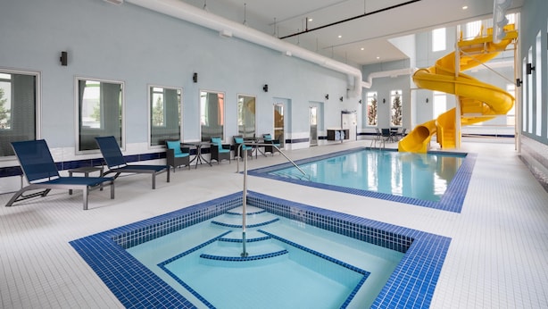A large indoor swimming pool with a yellow slide, lounge chairs, and a tiled floor. - Best Western Premier Executive Residency Medicine Hat (Medicine Hat)