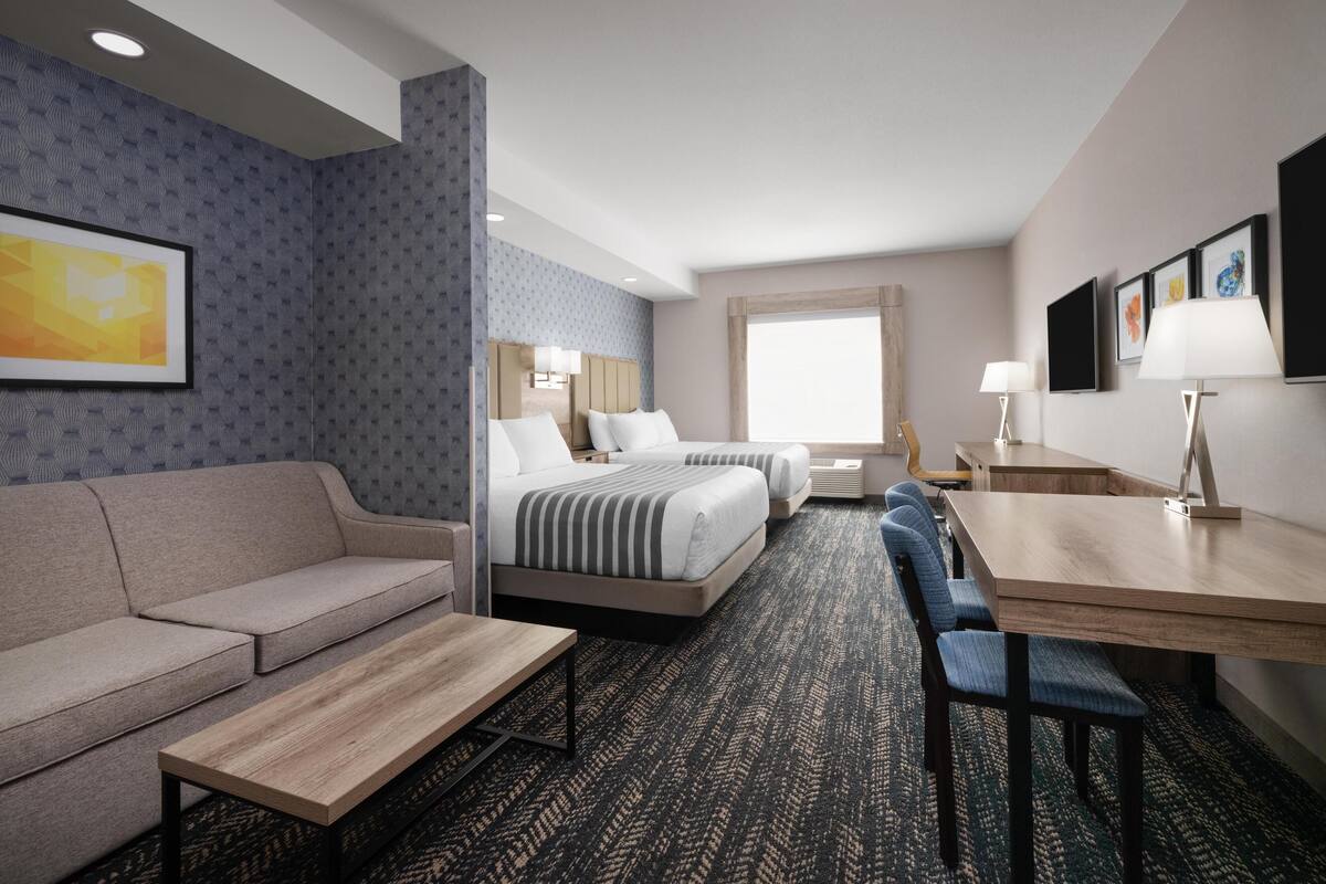 A hotel room with a sofa, two beds, a desk, and a chair.