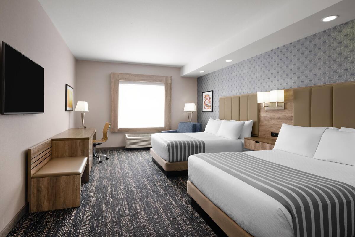 A hotel room with two beds, a desk, a chair, a flat-screen TV, and a window.