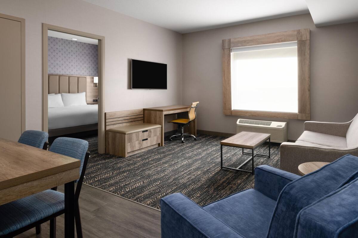 A hotel room with a bed, desk, chair, sofa, TV, and window.