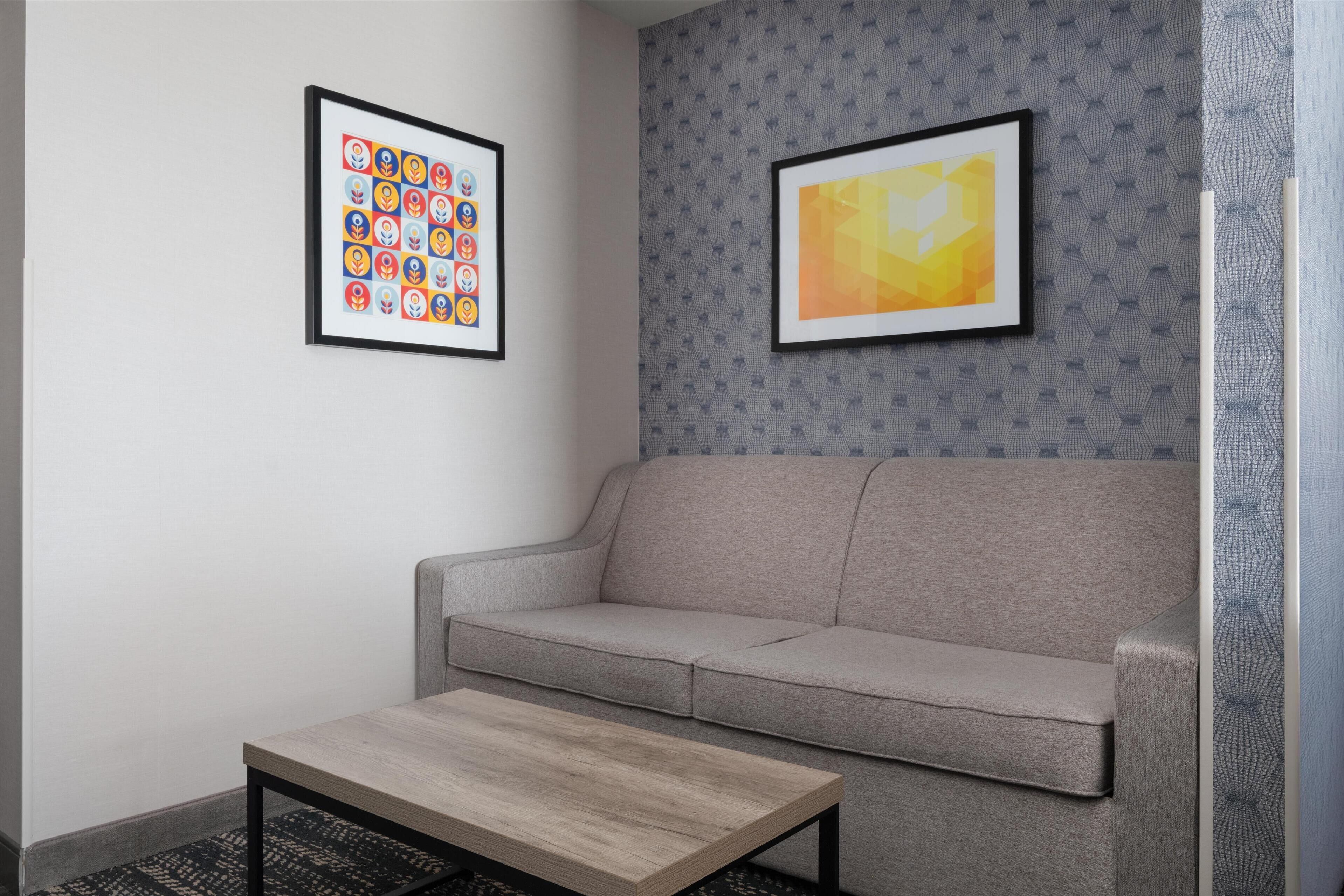 A modern room with a grey sofa, a wooden coffee table, and two framed artworks on the wall.