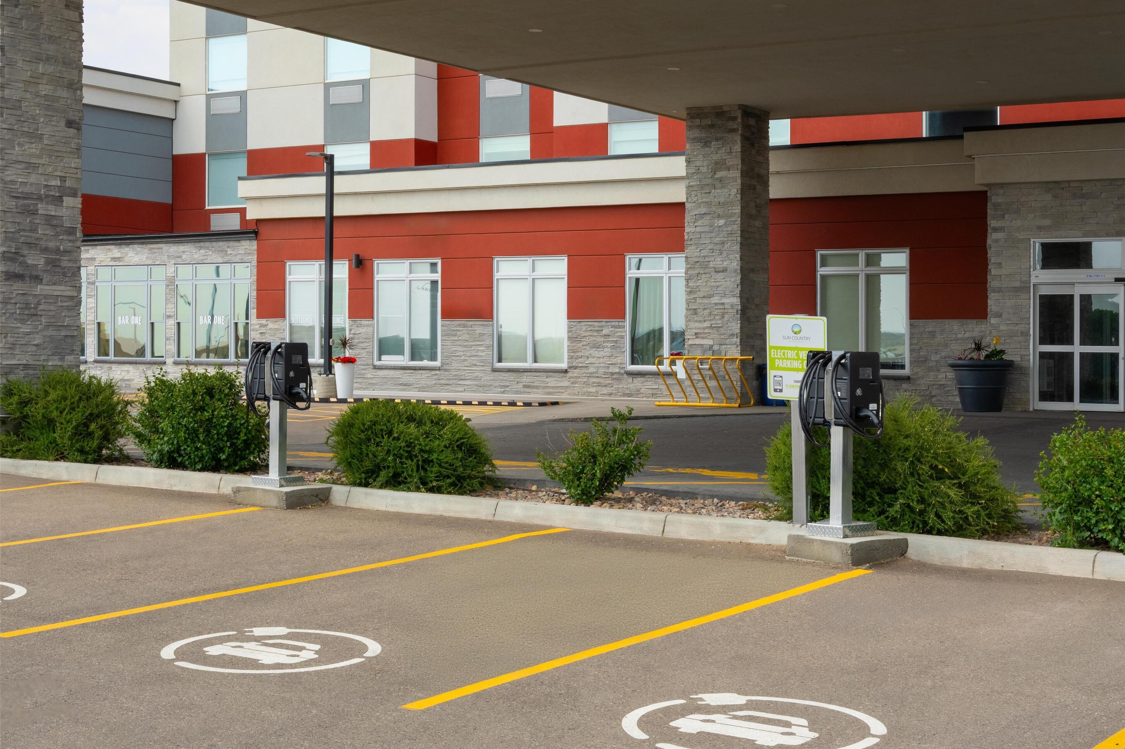 A parking area with electric vehicle charging stations, a building with a modern facade, and a sign indicating electric vehicle parking.