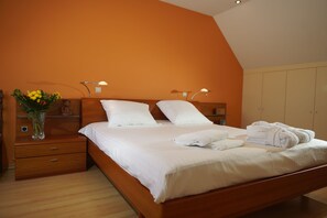 Un dormitorio con cama de madera, ropa de cama blanca, mesita de noche con un florero y un armario.