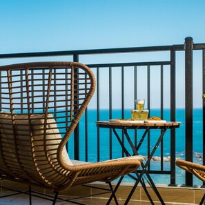 Ein Korbstuhl und ein kleiner Tisch mit Getränken und Snacks auf einem Balkon mit Blick aufs Meer.