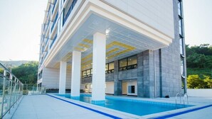 Un edificio moderno con zona de piscina, que incluye una sección cubierta con columnas y una piscina azul cristalina.