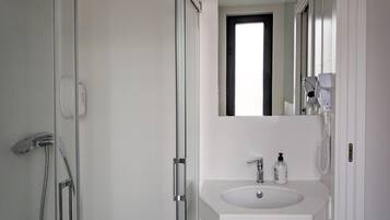 Un baño moderno con cabina de ducha de vidrio, un lavabo blanco con espejo y un secador de pelo en la pared.