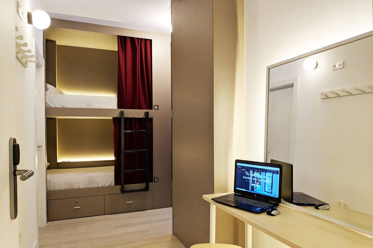 A hotel room with bunk beds, a desk with a laptop, and a mirror.