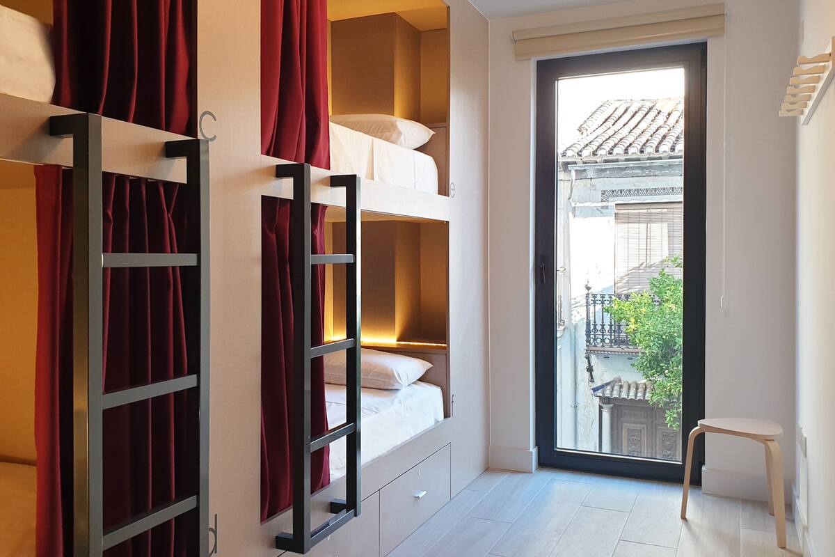 A dormitory-style room with bunk beds, a sliding door to a balcony, and a small table.
