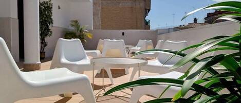 Una terrazza sul tetto con sedie di plastica bianca e un tavolo rotondo, circondata da piante in vaso.