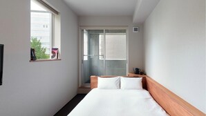 Ein Hotelzimmer mit Bett, Fenster, einer Tür, die auf einen Balkon führt, und einem kleinen Tisch mit Wasserkocher und Tasse.