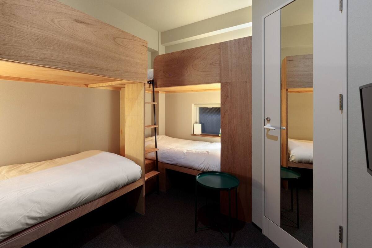 A dormitory room with two bunk beds, a small table, and a mirror.
