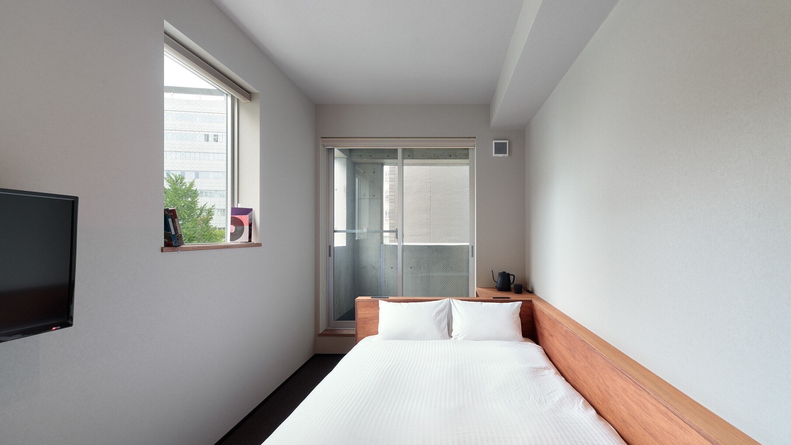 A hotel room with a bed, a TV, a window, and a door leading to a balcony.