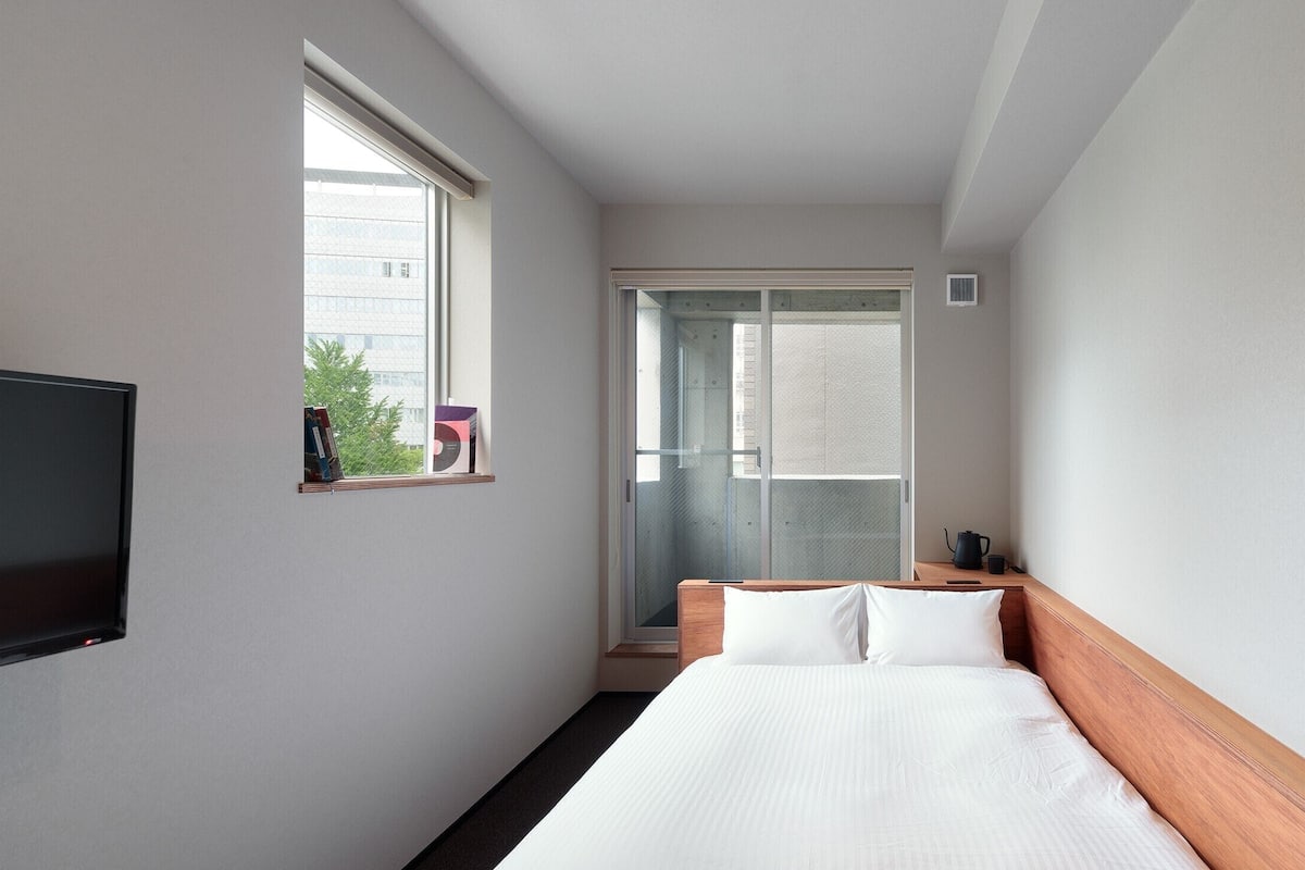 A hotel room with a bed, a TV, a window, and a door leading to a balcony.