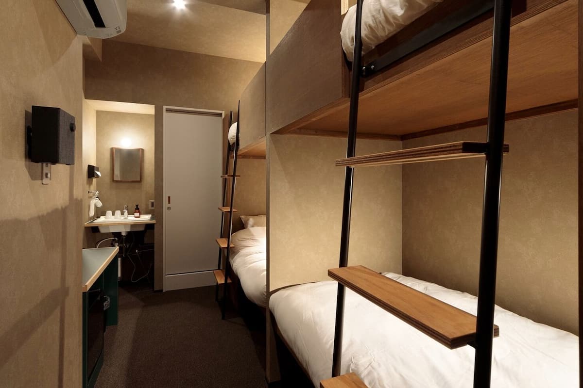 A dormitory room with bunk beds, a small sink, and a mirror.