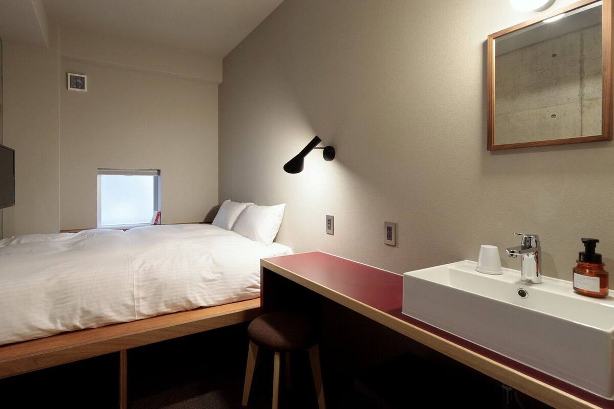 A compact hotel room with a bed, a desk, a sink, and a mirror.
